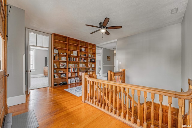 hall featuring baseboards, light wood-type flooring, an upstairs landing, and a textured ceiling