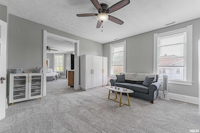 carpeted living area with a wealth of natural light, a ceiling fan, visible vents, a textured ceiling, and beverage cooler
