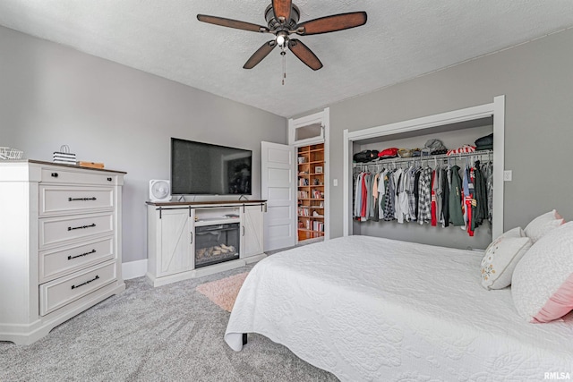 bedroom featuring carpet floors, a closet, a glass covered fireplace, a ceiling fan, and a textured ceiling