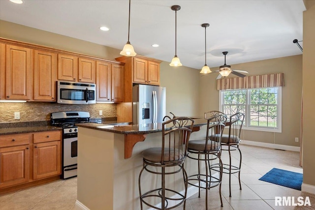kitchen featuring light tile patterned floors, tasteful backsplash, appliances with stainless steel finishes, a breakfast bar, and an island with sink