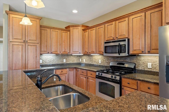 kitchen with dark stone counters, a sink, brown cabinets, stainless steel appliances, and decorative light fixtures