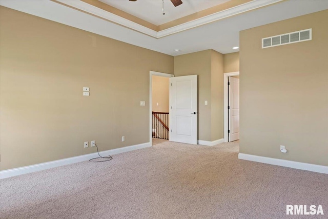 carpeted empty room featuring visible vents, ceiling fan, a raised ceiling, and baseboards