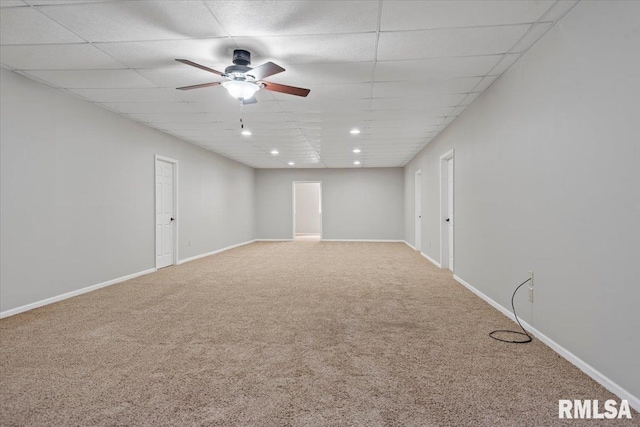 carpeted empty room featuring ceiling fan, a drop ceiling, and baseboards
