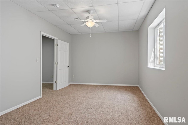 carpeted empty room featuring a ceiling fan, a drop ceiling, and baseboards