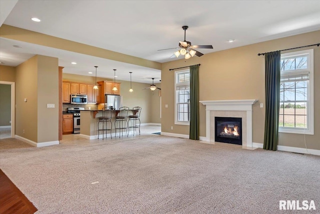 living room featuring ceiling fan, a wealth of natural light, light carpet, and baseboards