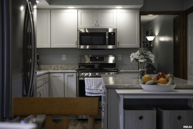kitchen with light stone countertops, white cabinetry, wood finished floors, and appliances with stainless steel finishes