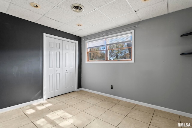 unfurnished bedroom featuring visible vents, light tile patterned floors, a closet, and a drop ceiling
