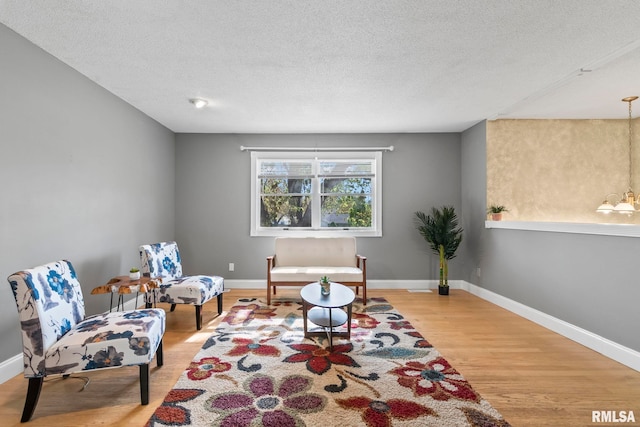 sitting room featuring baseboards, a notable chandelier, light wood-style floors, and a textured ceiling