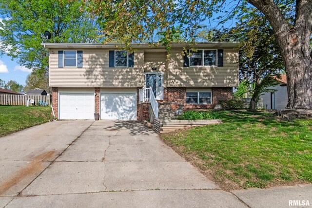 raised ranch with a front lawn, driveway, an attached garage, and brick siding