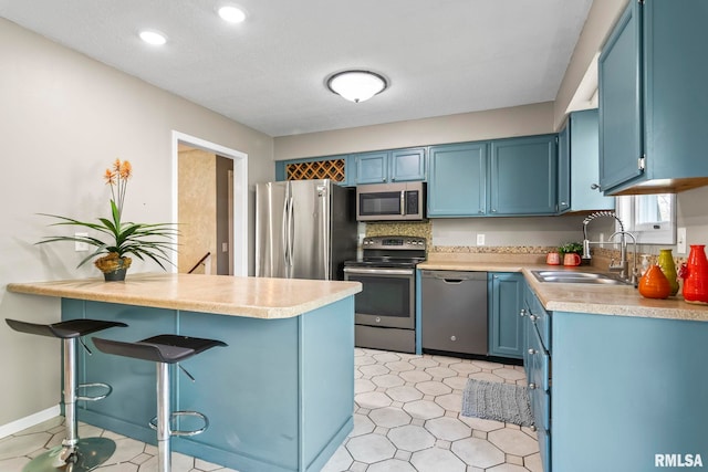 kitchen featuring a kitchen breakfast bar, a sink, stainless steel appliances, blue cabinetry, and a peninsula