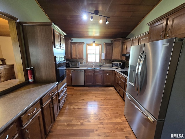 kitchen featuring a sink, decorative backsplash, light wood-style floors, black appliances, and wood ceiling