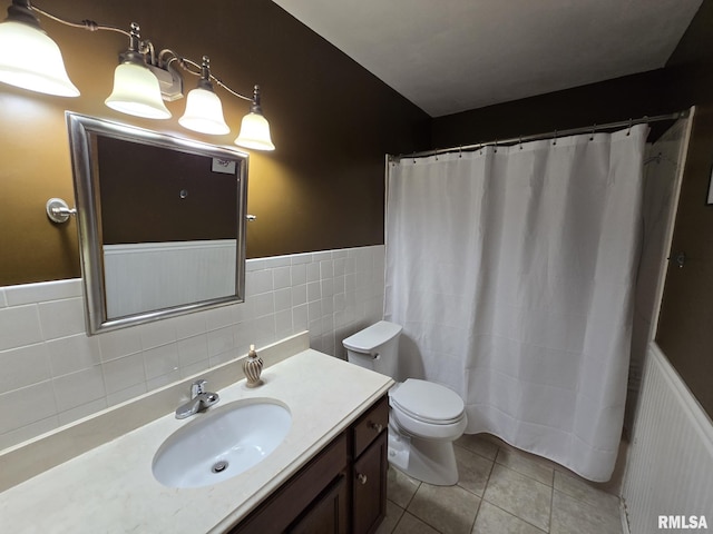 full bath with toilet, tile walls, tile patterned floors, vanity, and wainscoting