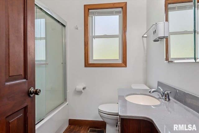 bathroom with wood finished floors, vanity, baseboards, toilet, and shower / bath combination with glass door