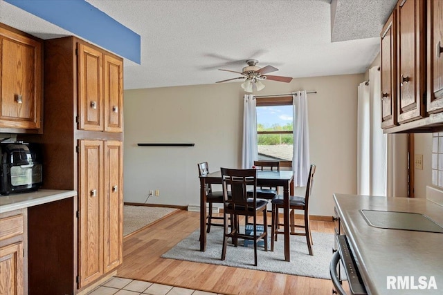 dining room featuring baseboards, ceiling fan, a textured ceiling, and light wood-style flooring