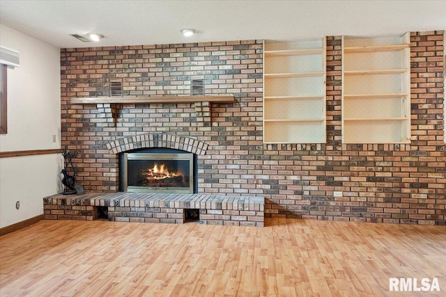unfurnished living room featuring a textured ceiling, visible vents, baseboards, a fireplace, and wood finished floors