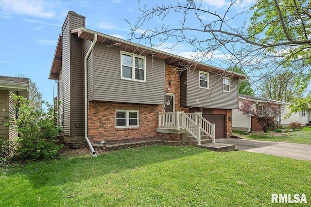 split foyer home featuring driveway, a chimney, a front yard, brick siding, and a garage