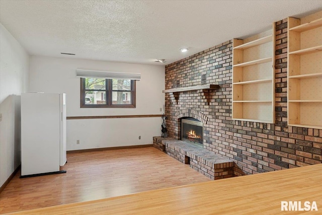 unfurnished living room featuring baseboards, wood finished floors, a textured ceiling, and a fireplace