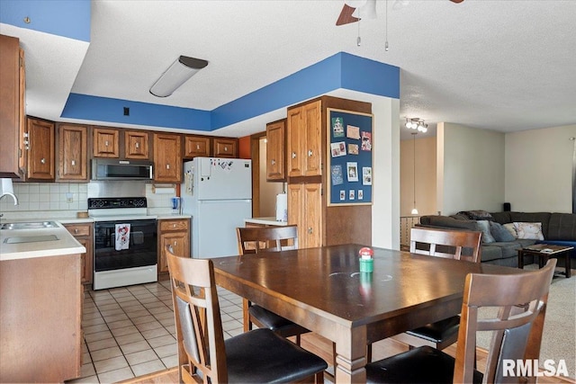 kitchen with freestanding refrigerator, brown cabinetry, electric range, light countertops, and a sink