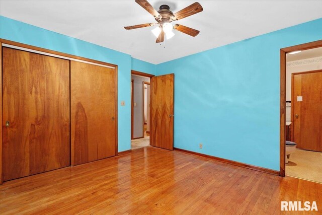 unfurnished bedroom featuring ensuite bath, a ceiling fan, baseboards, wood finished floors, and a closet
