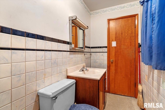 half bathroom with vanity, a wainscoted wall, toilet, and tile walls