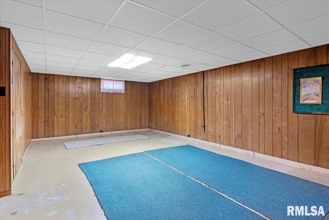 interior space with a drop ceiling and wooden walls