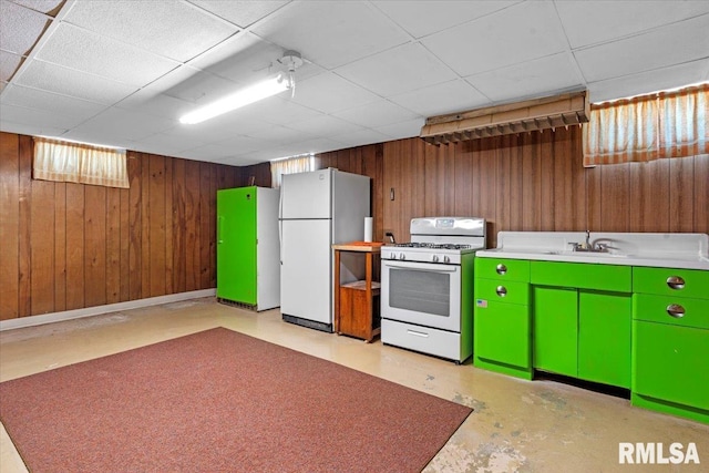 kitchen with wood walls, concrete flooring, white appliances, a paneled ceiling, and a sink