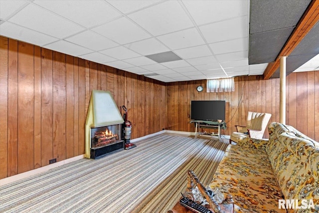 carpeted living room with a drop ceiling and wood walls