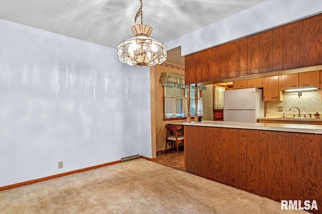 kitchen with decorative backsplash, light colored carpet, light countertops, freestanding refrigerator, and an inviting chandelier