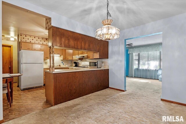 kitchen with light countertops, a peninsula, a notable chandelier, under cabinet range hood, and white appliances