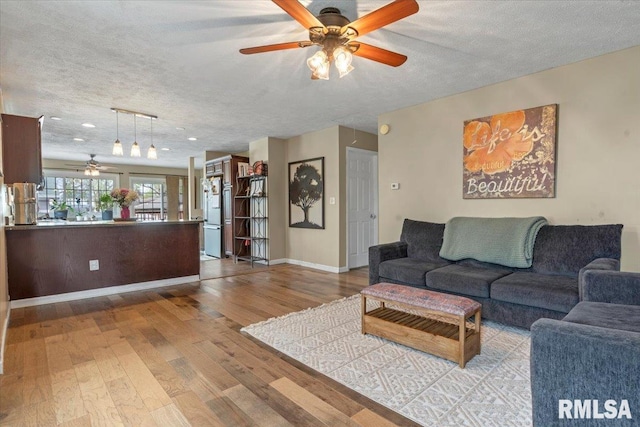 living area with wood finished floors, ceiling fan, baseboards, and a textured ceiling