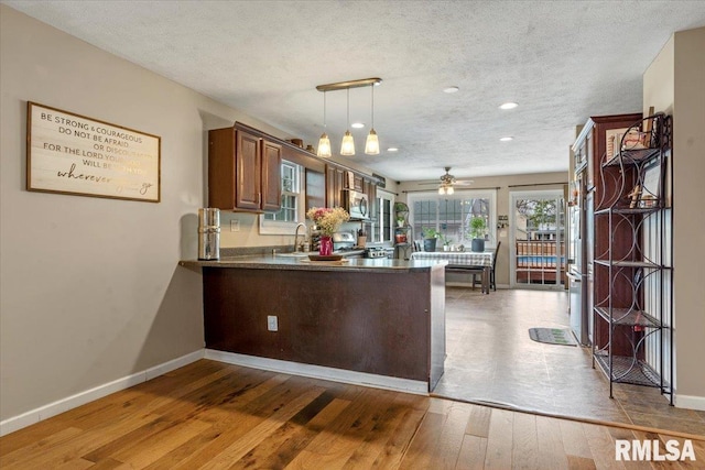 kitchen featuring stainless steel microwave, a peninsula, baseboards, dark countertops, and hardwood / wood-style flooring