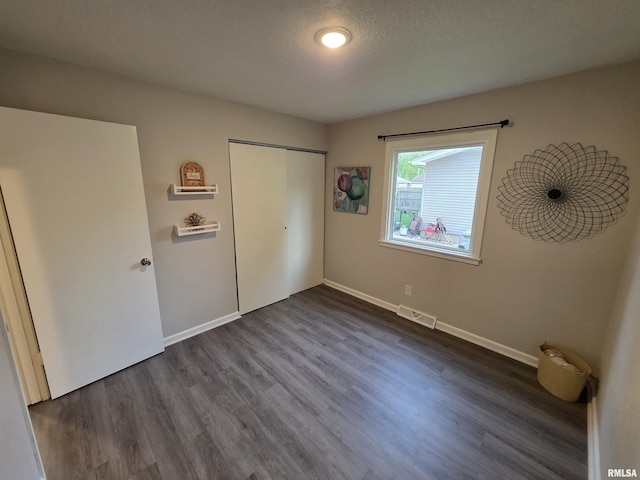 unfurnished bedroom featuring dark wood-style flooring, visible vents, a closet, and baseboards