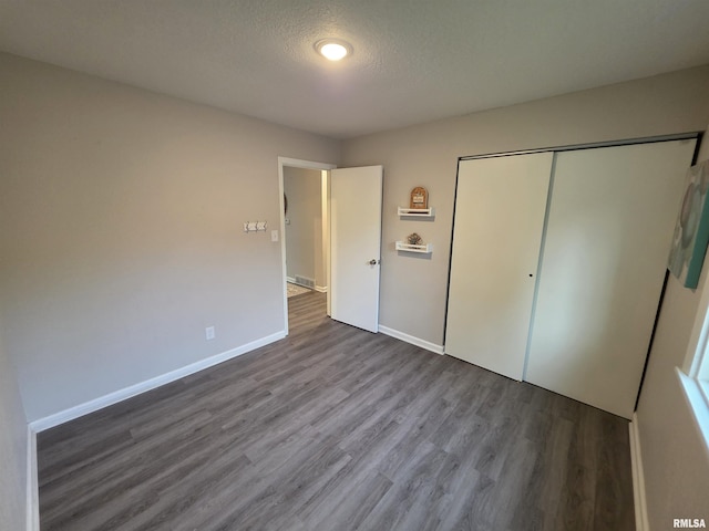unfurnished bedroom with a textured ceiling, wood finished floors, baseboards, and a closet