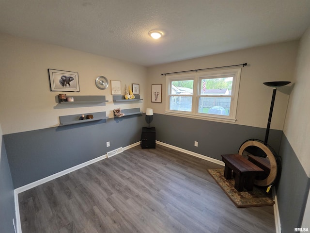 interior space featuring a textured ceiling, wood finished floors, visible vents, and baseboards