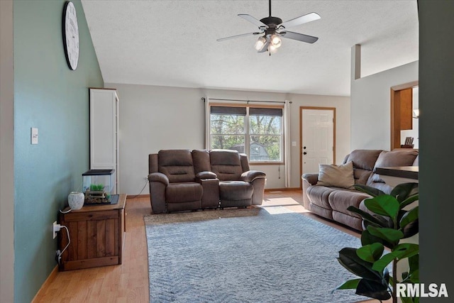 living area with ceiling fan, a textured ceiling, vaulted ceiling, baseboards, and light wood-style flooring