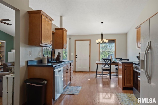 kitchen with brown cabinetry, dark countertops, a sink, light wood finished floors, and stainless steel appliances