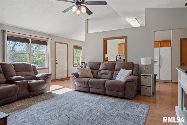 living area featuring light wood-type flooring, a textured ceiling, ceiling fan, and vaulted ceiling