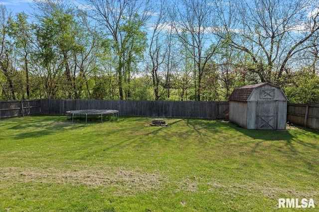 view of yard with a fenced backyard, an outbuilding, a trampoline, an outdoor fire pit, and a storage shed