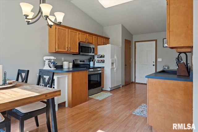 kitchen featuring brown cabinetry, dark countertops, lofted ceiling, stainless steel appliances, and light wood-style flooring