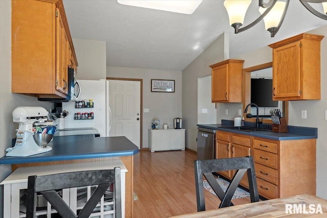 kitchen featuring lofted ceiling, brown cabinets, a sink, light wood-style flooring, and appliances with stainless steel finishes