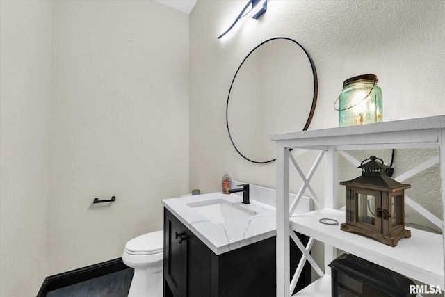 half bathroom with vanity, toilet, and baseboards