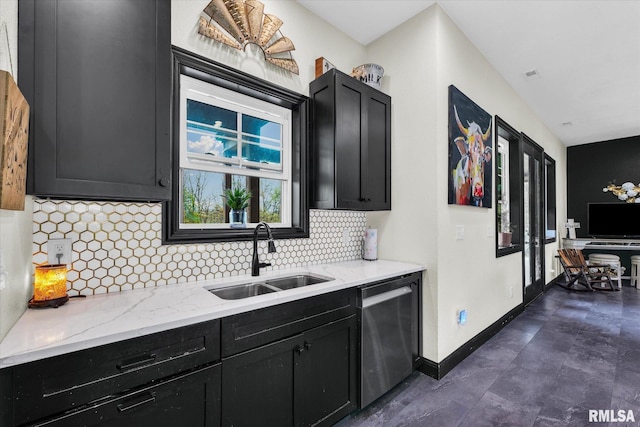 kitchen featuring a sink, tasteful backsplash, light stone counters, stainless steel dishwasher, and dark cabinets