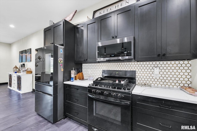 kitchen featuring black appliances, wood finished floors, backsplash, and dark cabinets