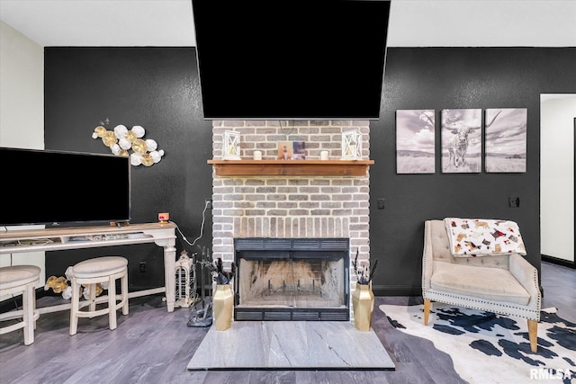 living area featuring wood finished floors, baseboards, and a brick fireplace