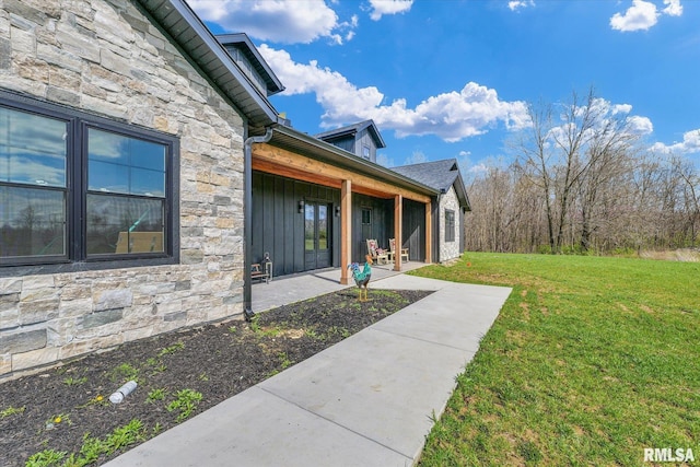 exterior space with a lawn, a patio, board and batten siding, and stone siding