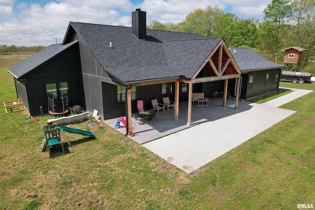 rear view of house with a chimney, board and batten siding, a patio, roof with shingles, and a lawn