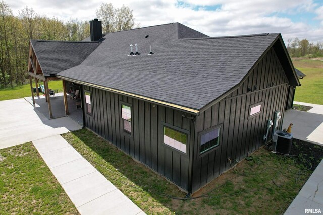 view of side of property featuring central AC, board and batten siding, a shingled roof, and a patio area