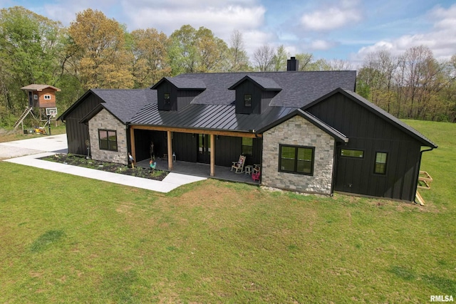 view of front facade featuring board and batten siding, a patio, stone siding, a standing seam roof, and a front lawn