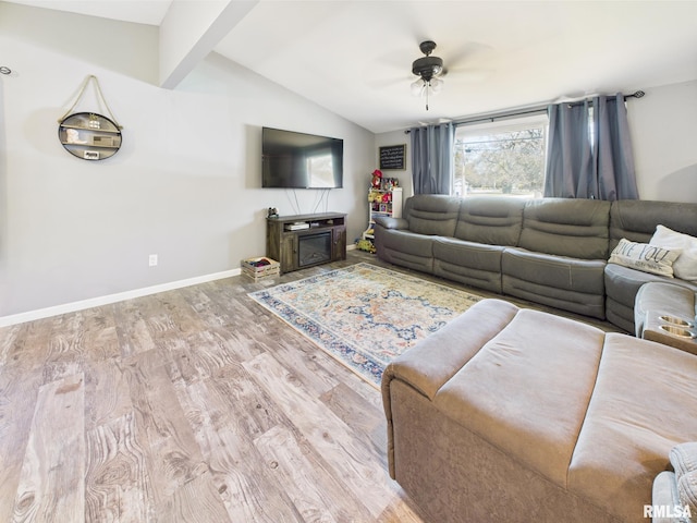 living area with vaulted ceiling with beams, wood finished floors, a fireplace, baseboards, and a ceiling fan