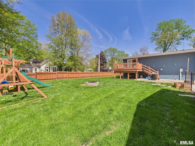 view of yard with a deck, a fire pit, a fenced backyard, and a playground